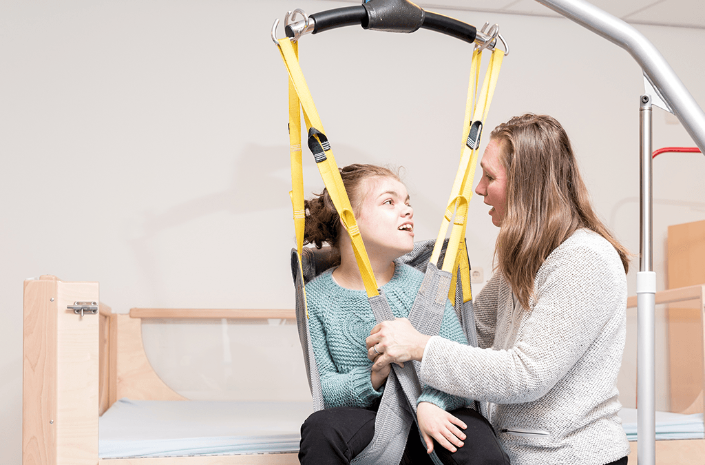 Photo of child in hoist with support worker assisting