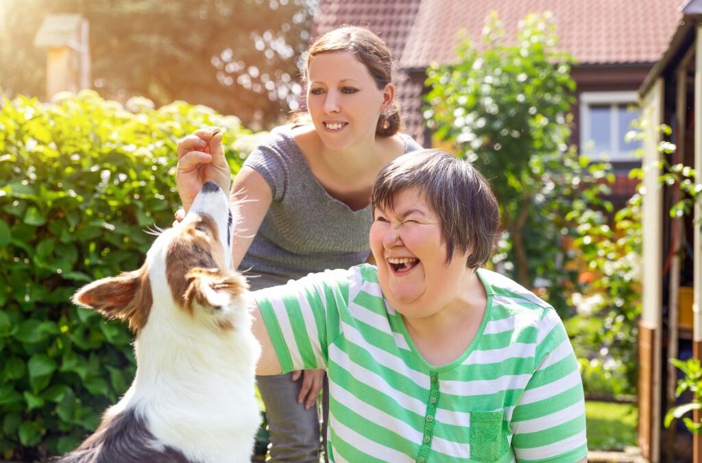 Photo of woman with an intellectual impairment and her guardian, playing with her dog in the backyard