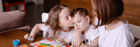 Photo of young boy with Cerebral Palsy finger painting with sister and mother