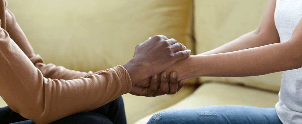 Photo of a black man holding hands with and comforting a black woman.