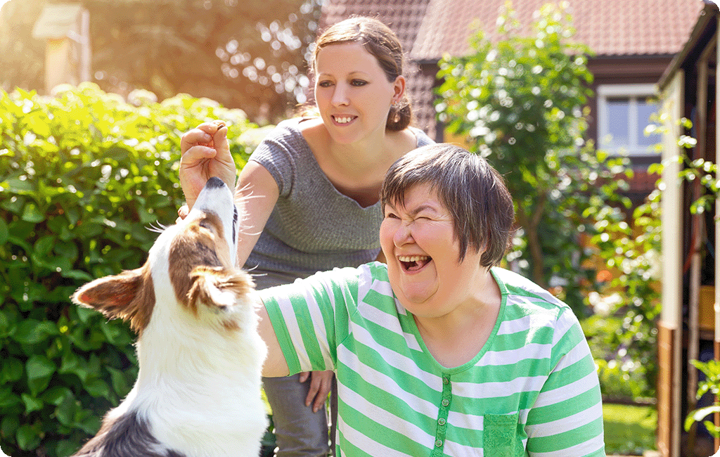 Woman with an intellectual impairment and another woman, playing with a dog in the backyard