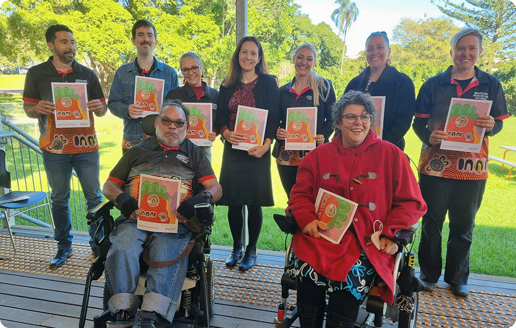 Photo of the 9 people from QAI’s Reconciliation Action Plan working group, all smiling and holding a copy of the new plan booklet.