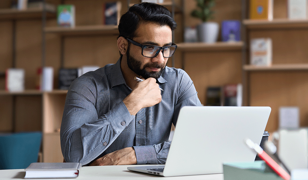 Professional young Indian man in his office reading something on his laptop.