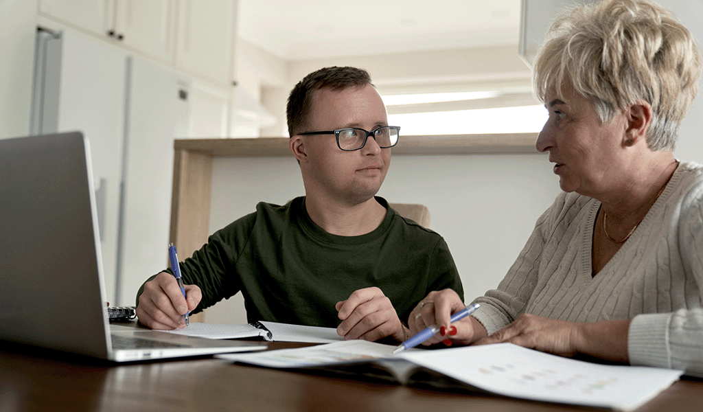 Man with Down Syndrome and his mum sitting at table with laptop and papers.