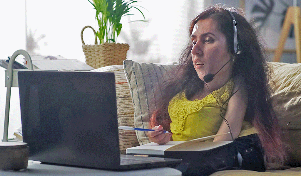 Woman with a disability sitting on a couch with a notebook and using speech to text on her laptop.
