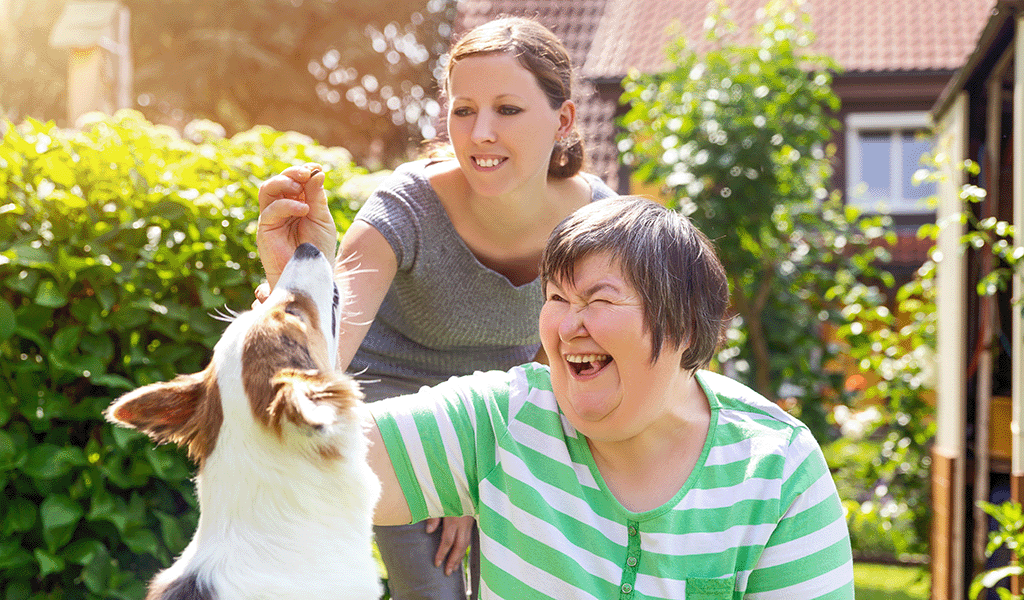 Woman with an intellectual impairment feeding her dog a treat with the help of her support worker.