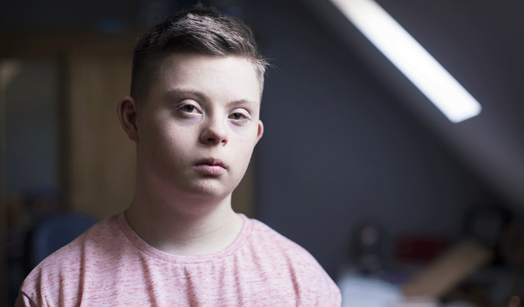 Young boy with Down Syndrome in his bedroom, with a sad expression on his face