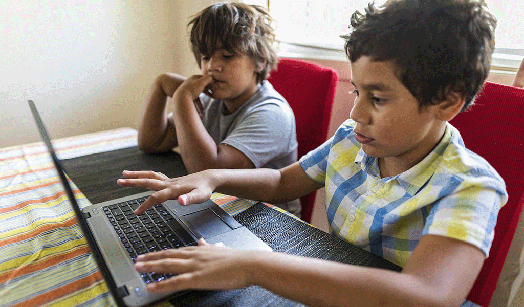 Two young Indigenous boys using a laptop at dining table
