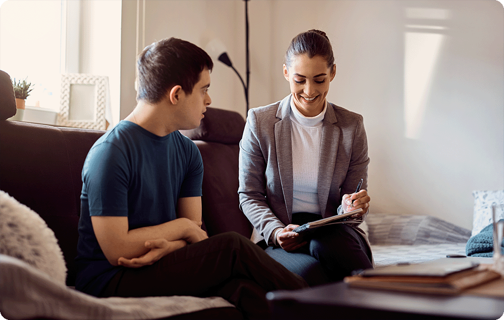 Allied health professional sitting on a couch with a client with disability talking through some papers