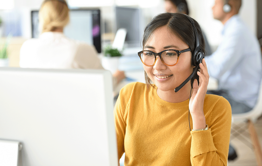 A woman wearing glasses and a headset is working on a computer